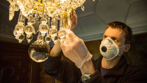 Staff member cleaning a chandelier at Lanhydrock, Cornwall